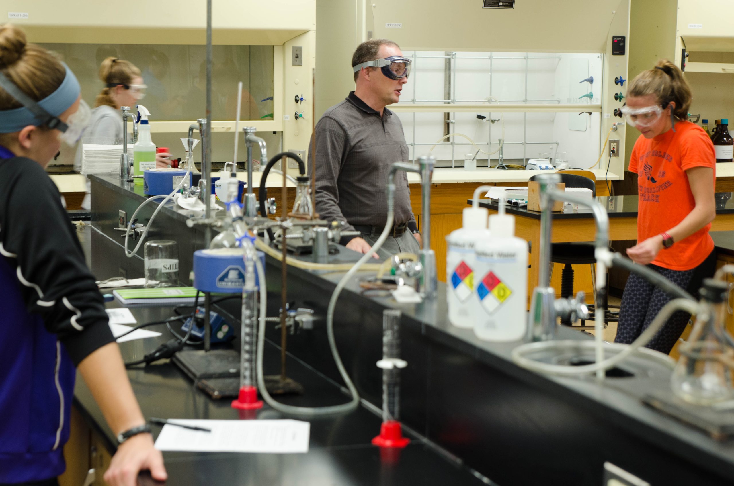 Teacher giving instructions to three students in chemistry lab