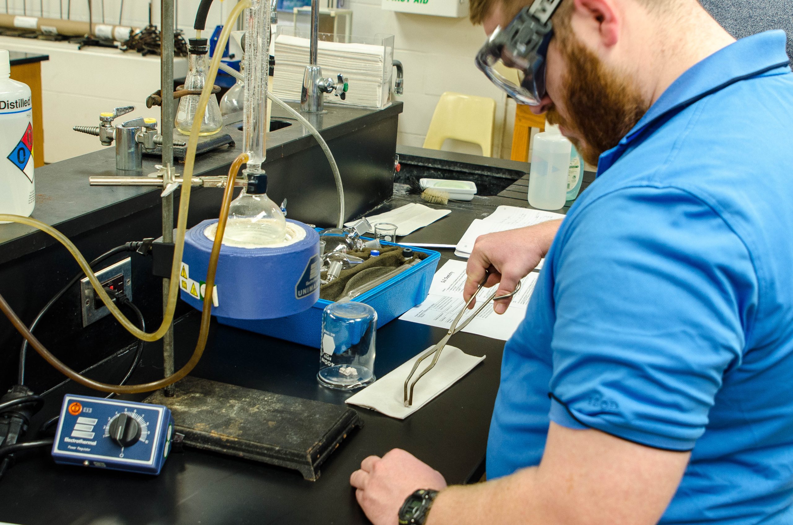 one male student in laboratory - wearing goggles and using tongs