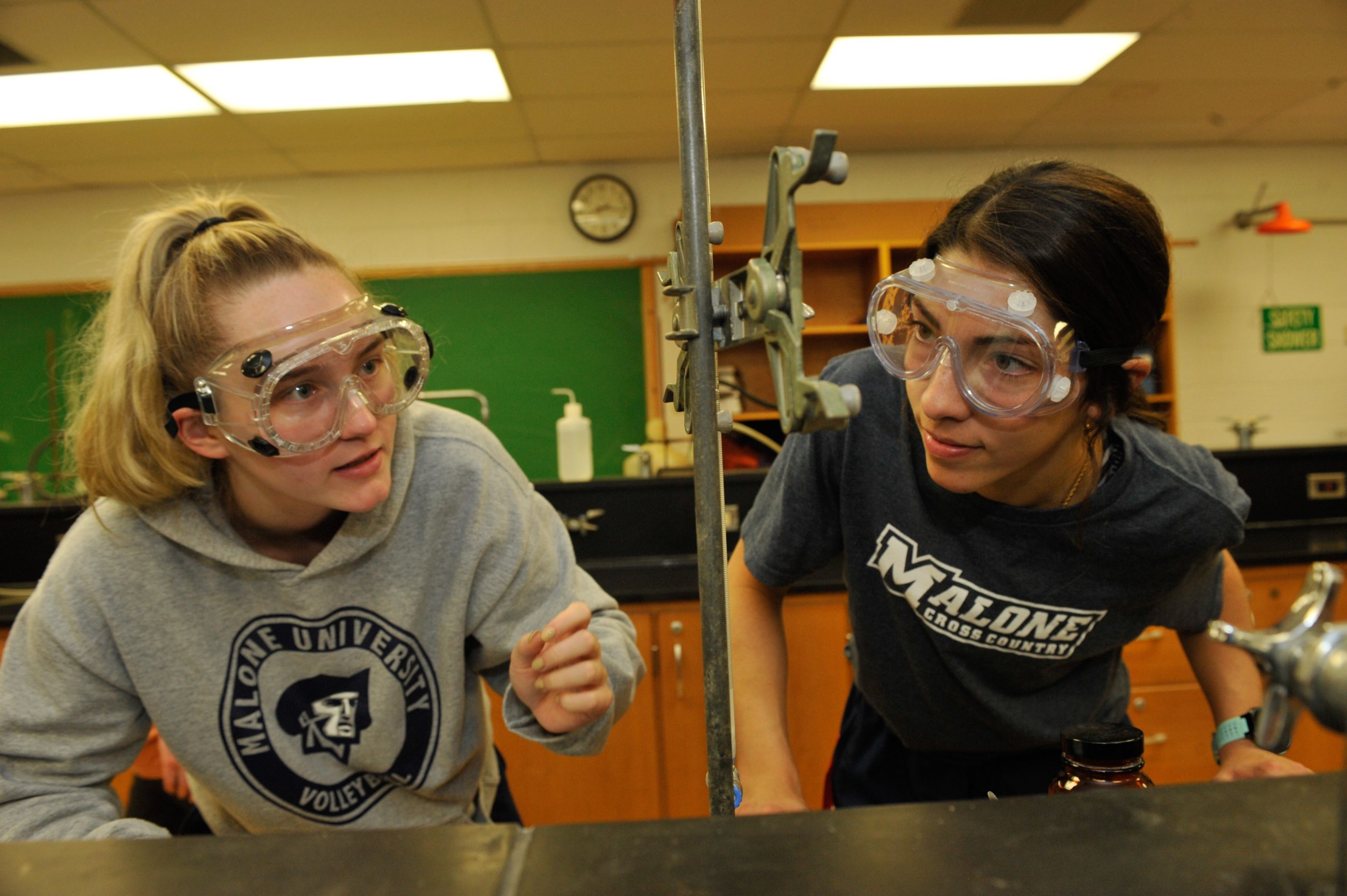 two female students with goggles looking intently at a piece of lab equipment