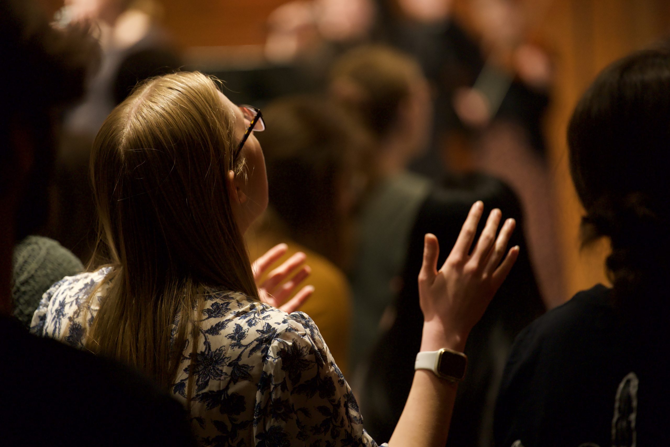 back side view of one female with hands raised in worship