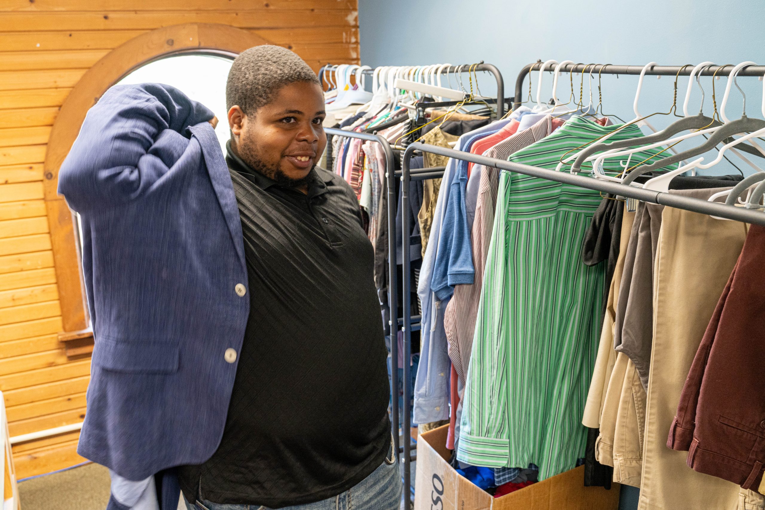 young male trying on a jacket in a room of clothing on racks