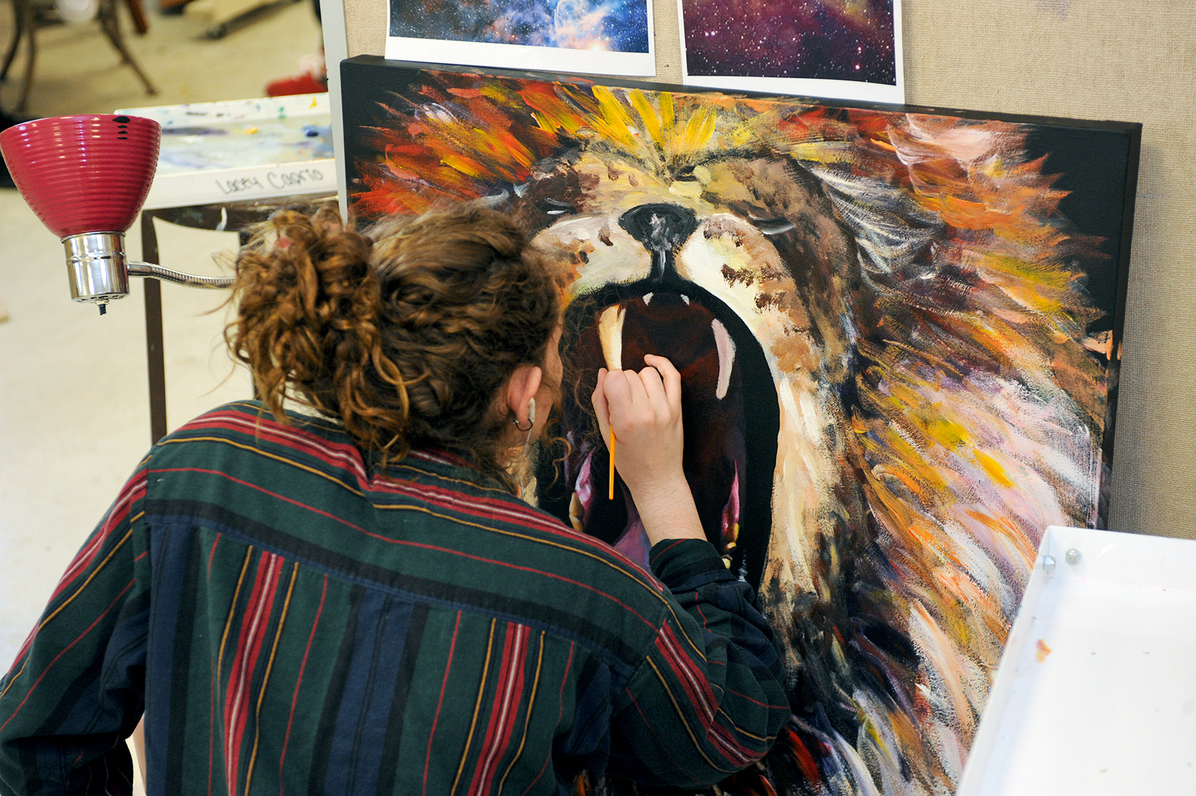 female student (from her back side) and her hand engaged in painting a large piece of artwork