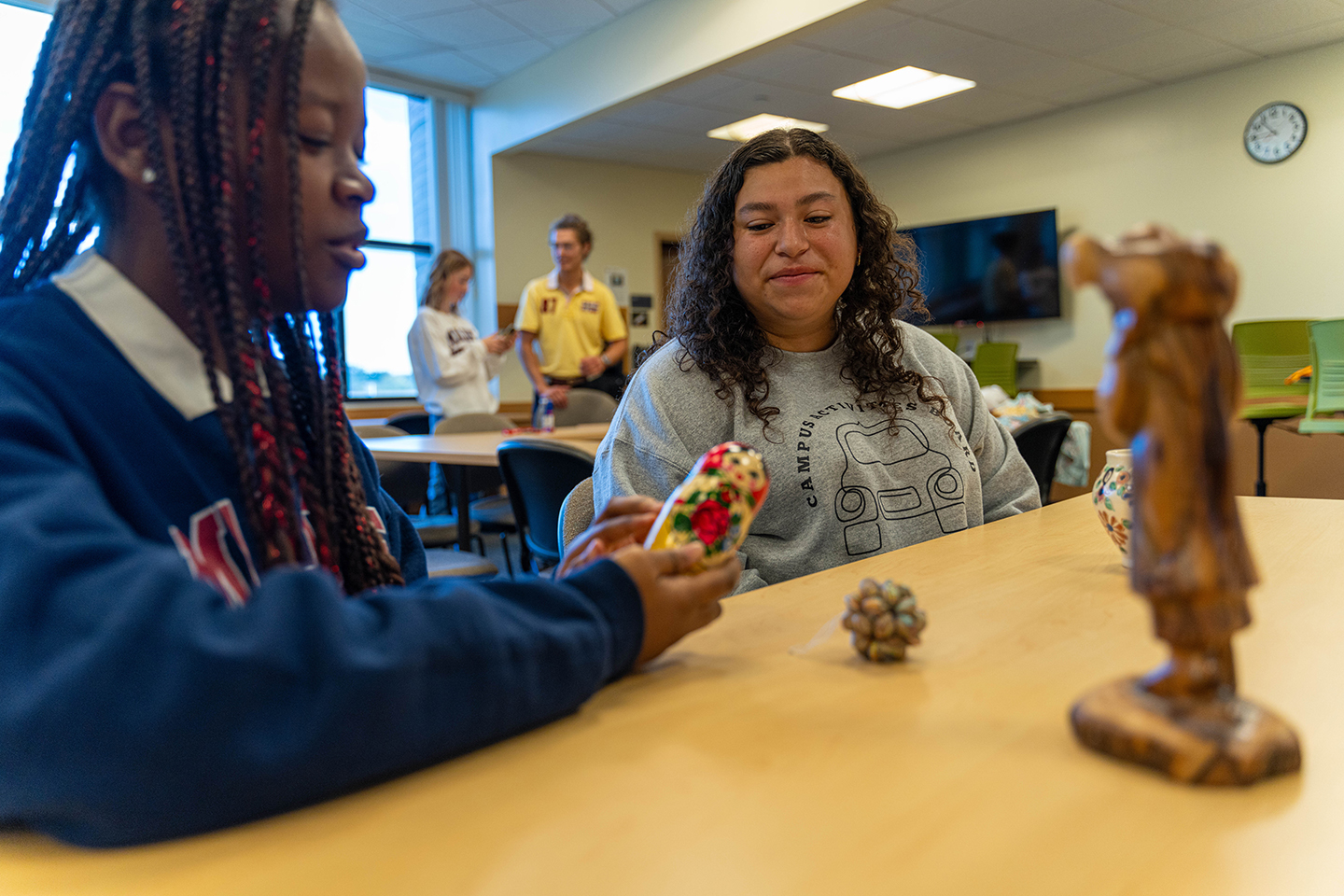 two female students examining international "trinkets" such as a set of nesting dolls
