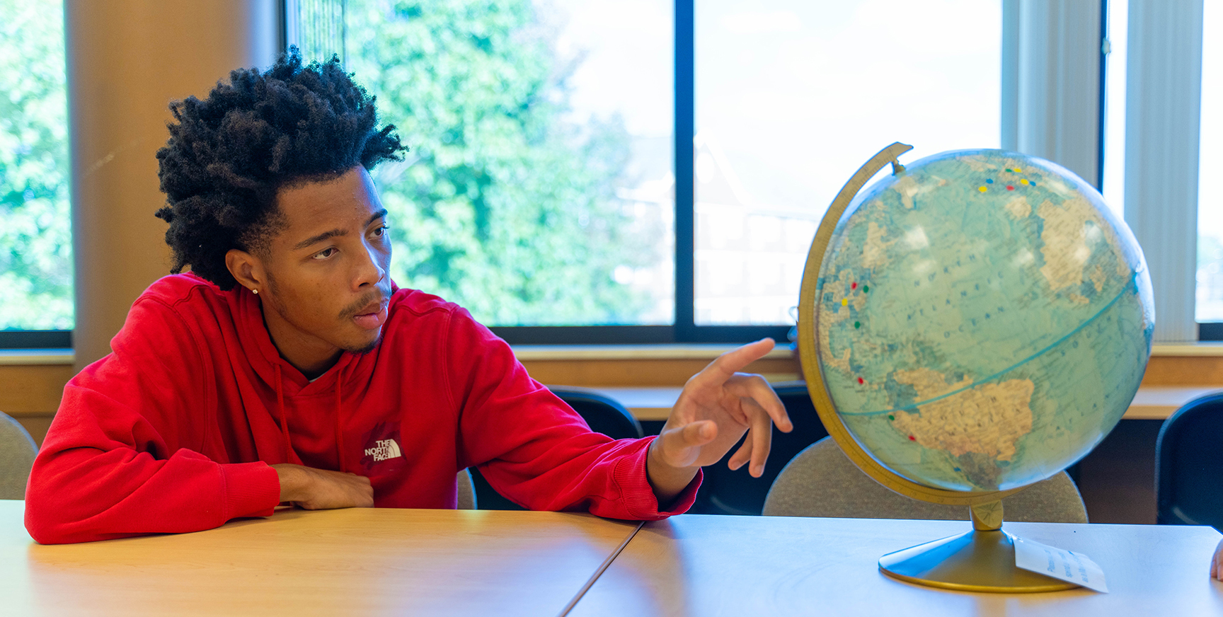 male student looking intently at a world globe
