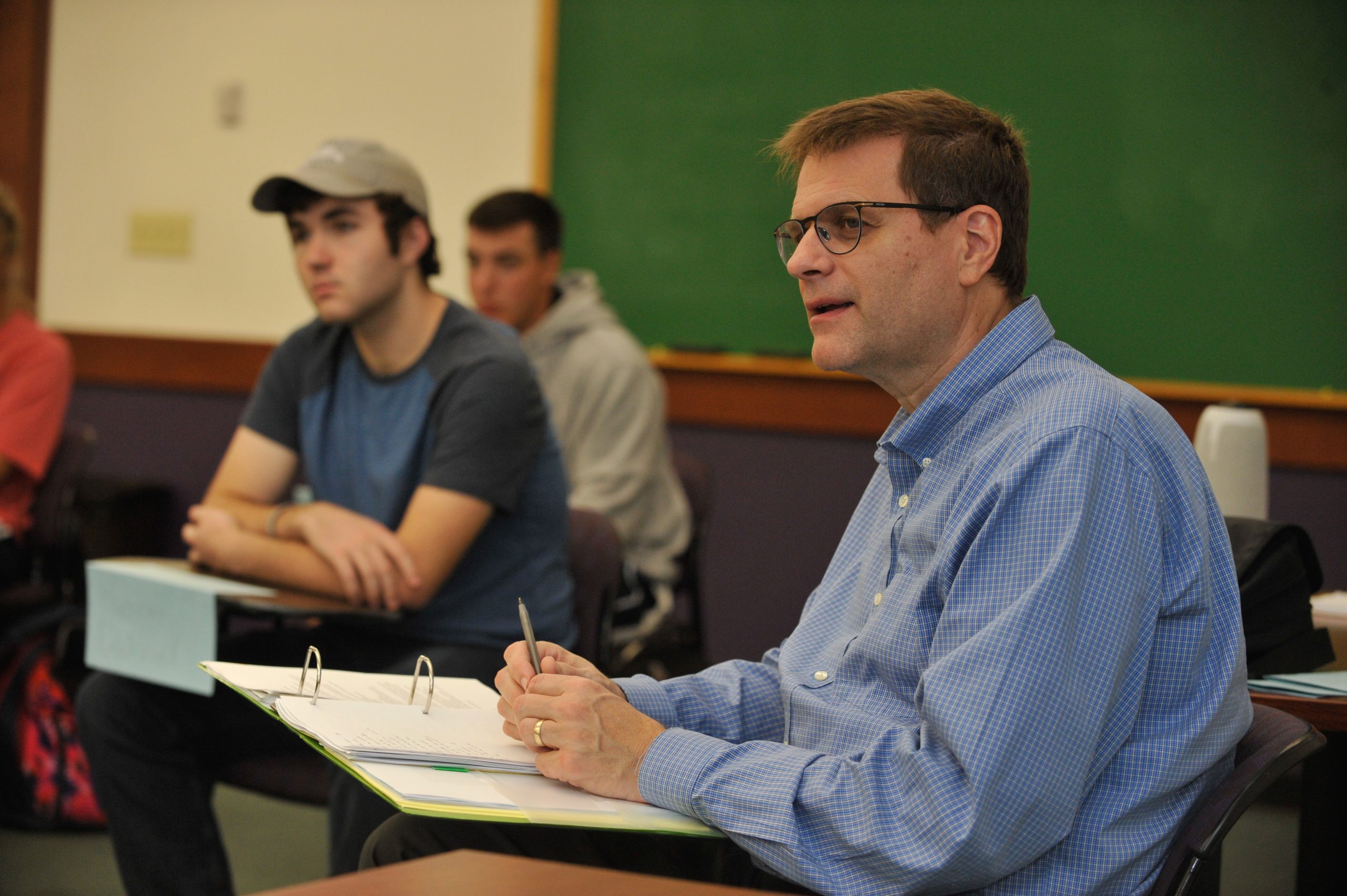 Professor Jay Case seated at desk among students - all appearing to be viewing a presentation