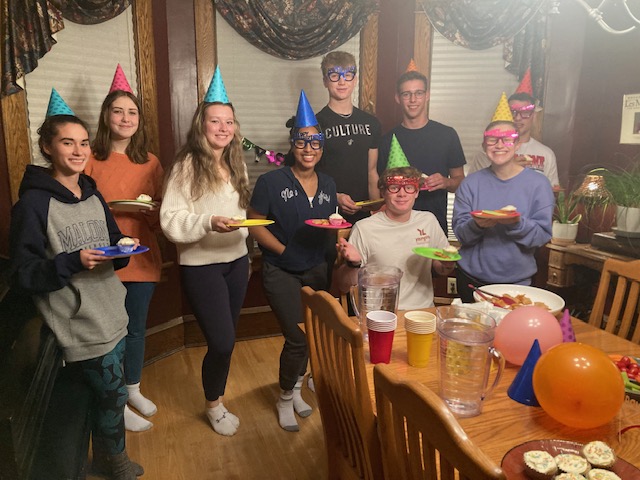 9 students wearing party gear and holding paper plates of refreshments