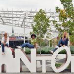 3 females seated atop outdoor large lettered platform spelling CANTON