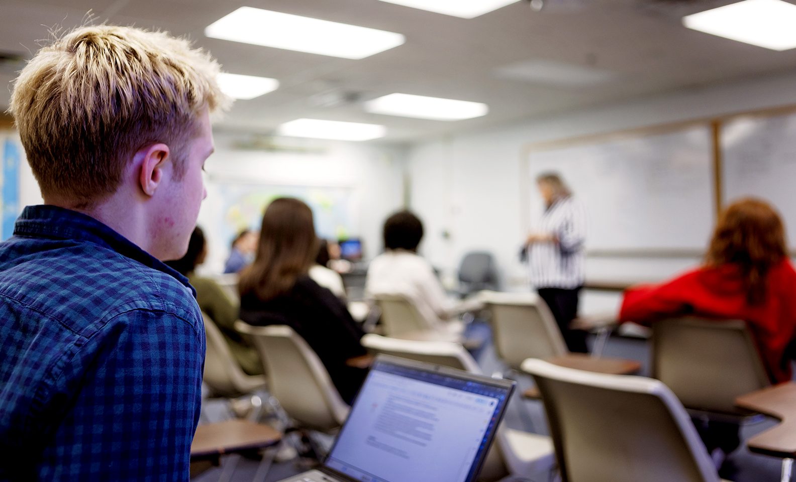 classroom scene; male student in foreground with open laptop