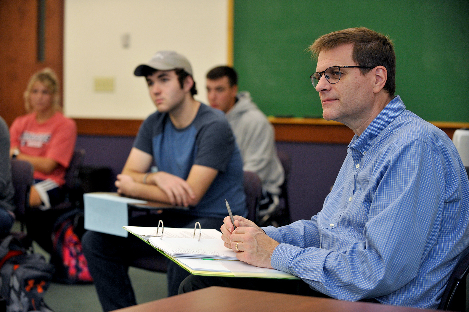 Jay Case seated in classroom among students. All appear to be watching a presentation.