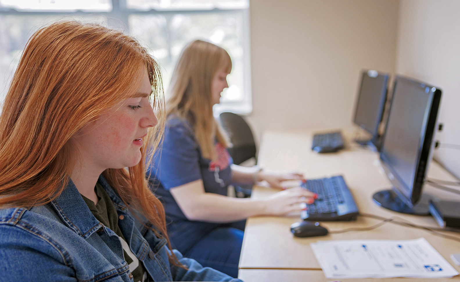 2 females seated in front of computers in lab