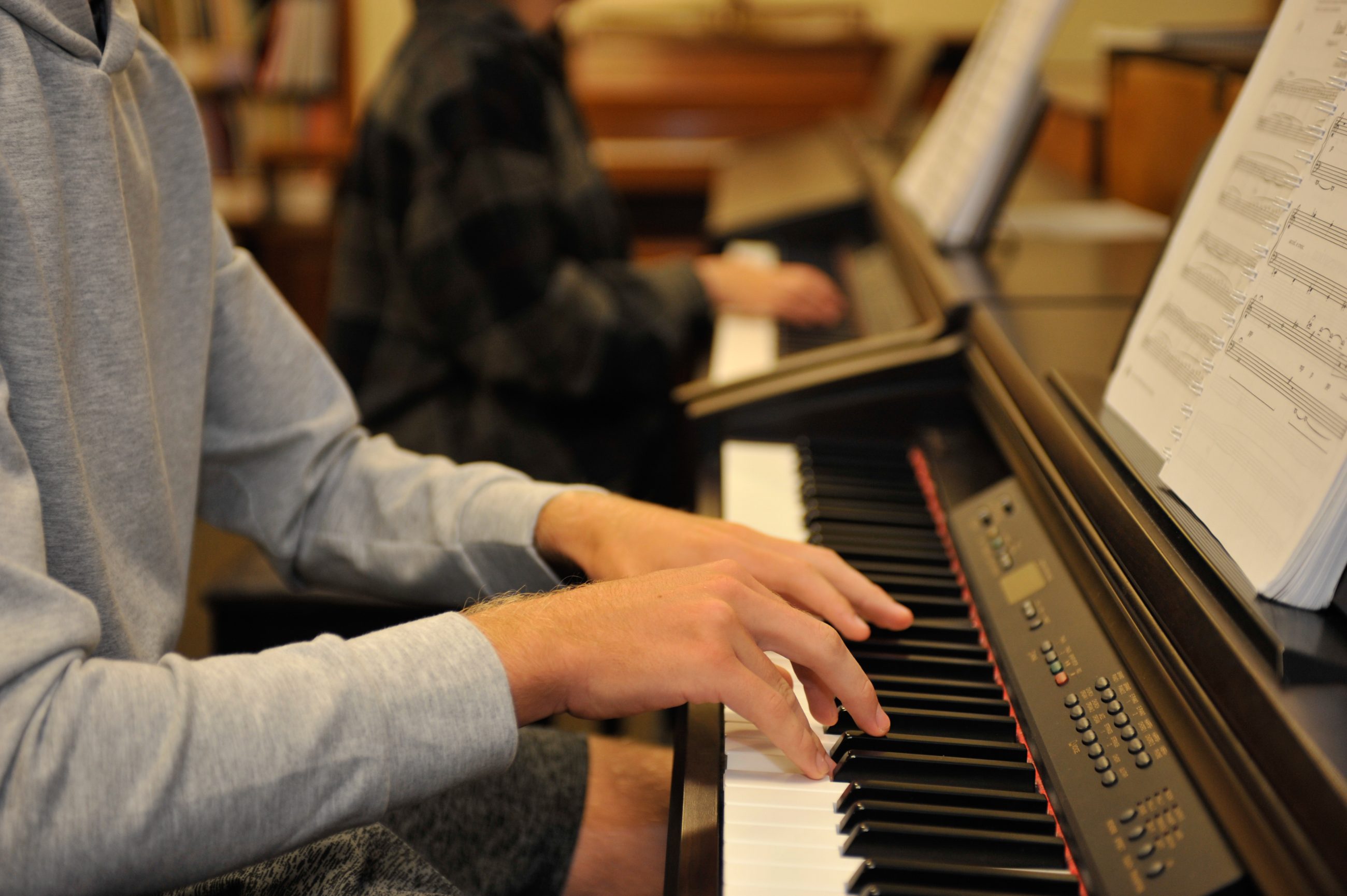 2 students at electronic keyboards with music on music racks