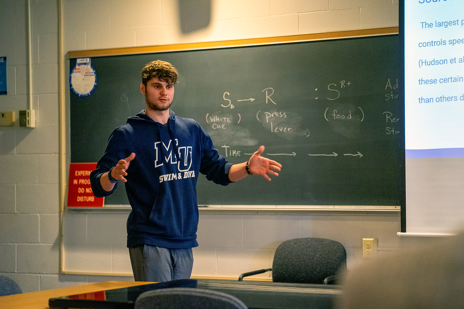 male student gesturing in front of chalkboard