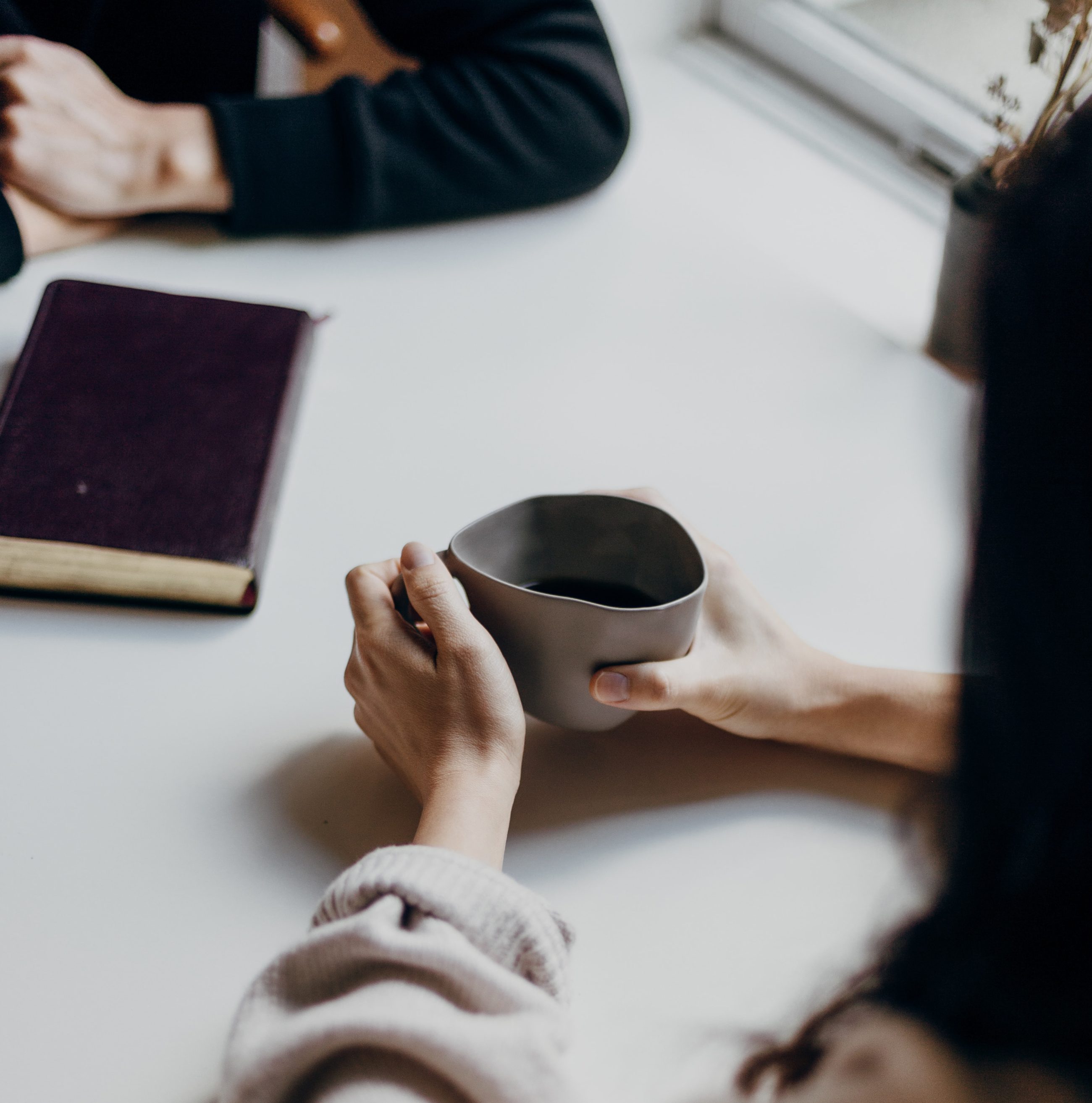 2 people (only partially visible) seated at table opposite each other, one holding beverage cup
