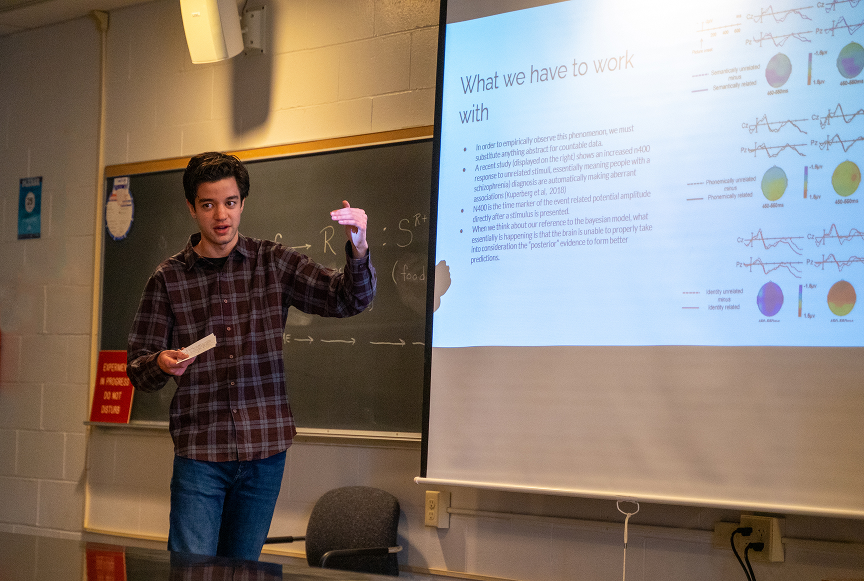 male student gesturing in front of image of psychology study information on projector screen