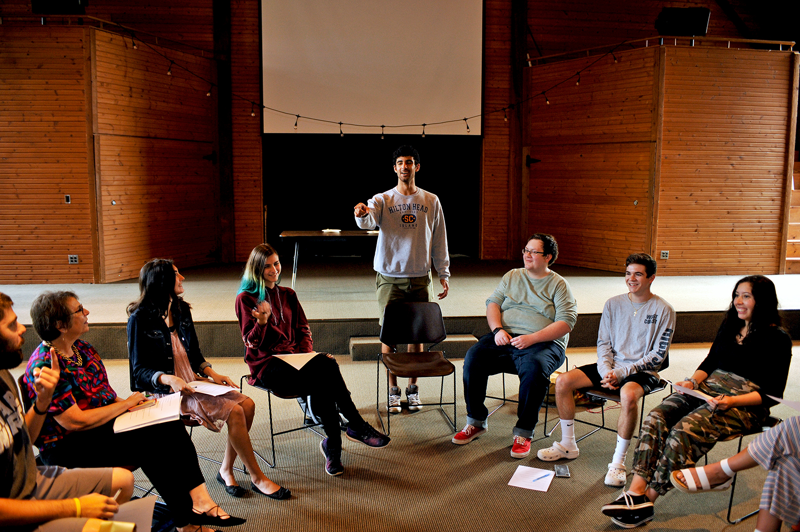 people seated in semi-circle in the Stewart Room with one student standing and gesturing toward group