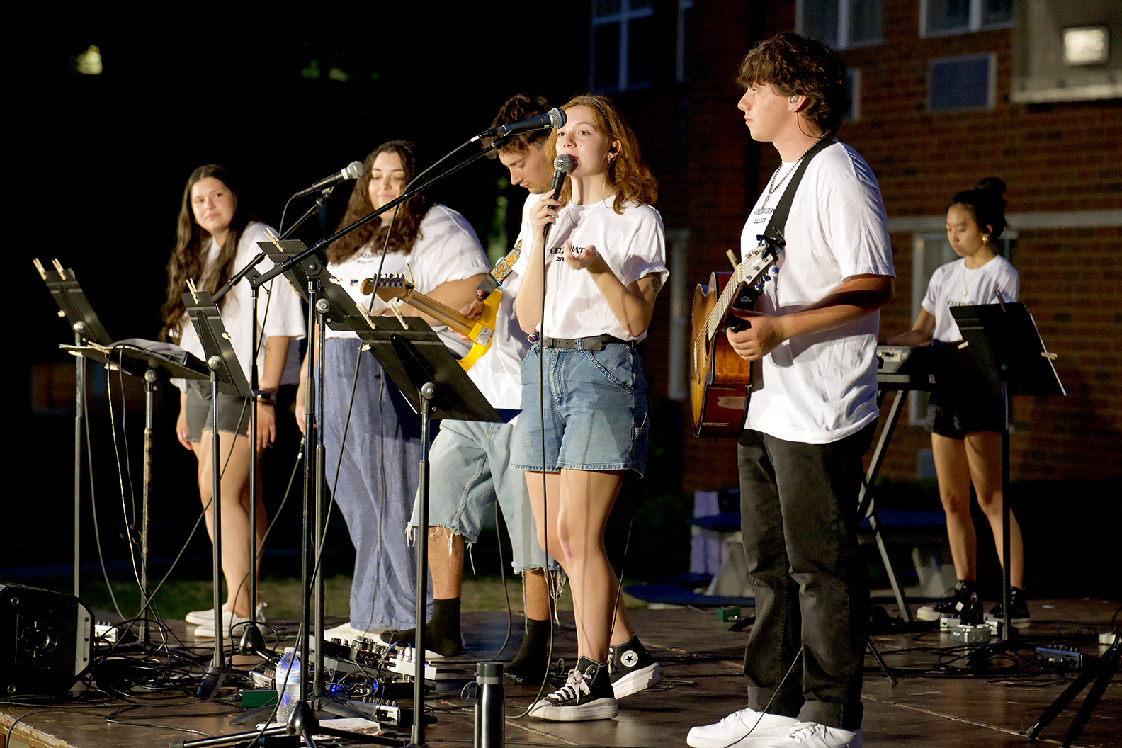 6 students leading music behind mics and music stands; 1 at a keyboard, 2 with guitars