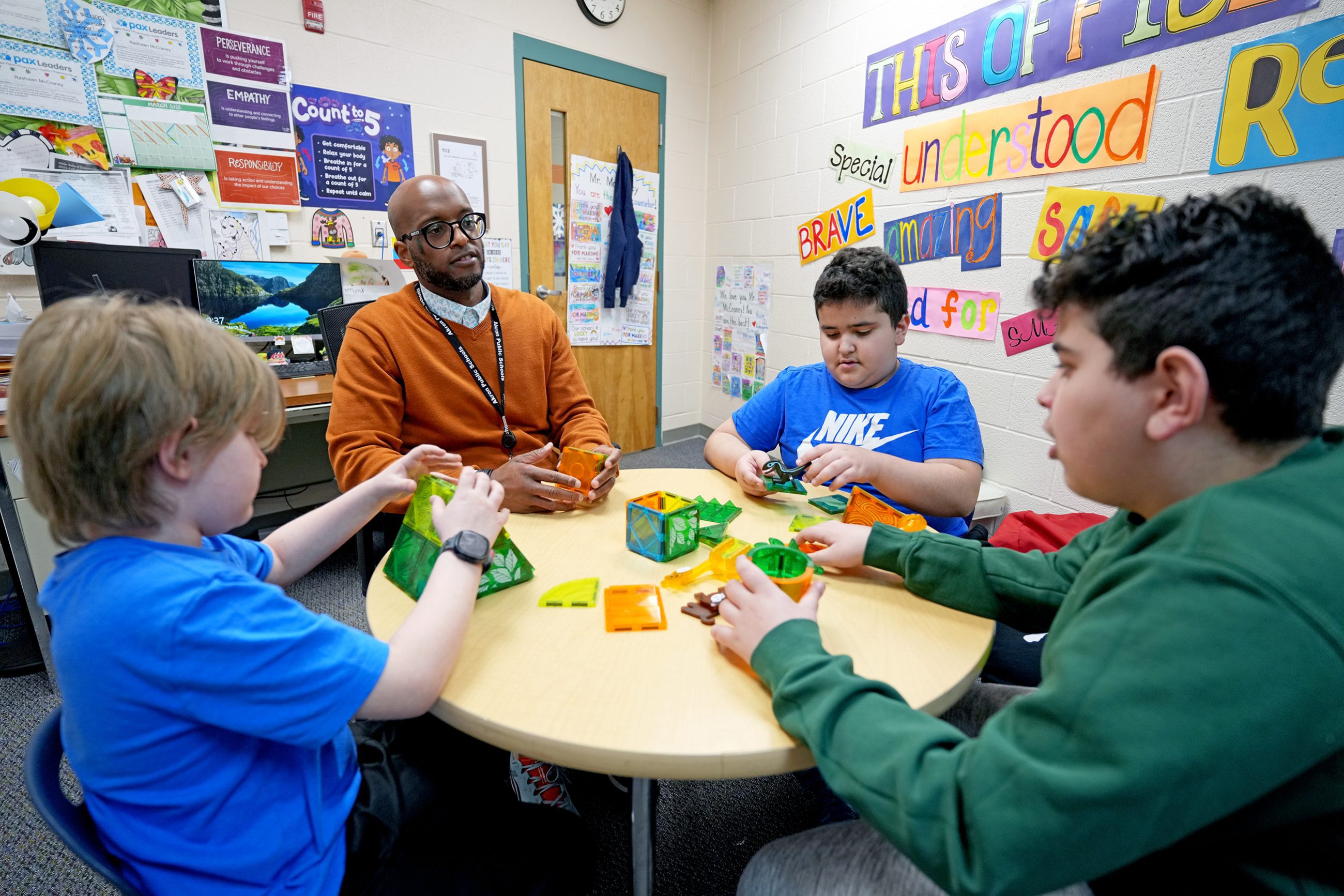 male counselor seated at round table with 3 young male students in a classroom