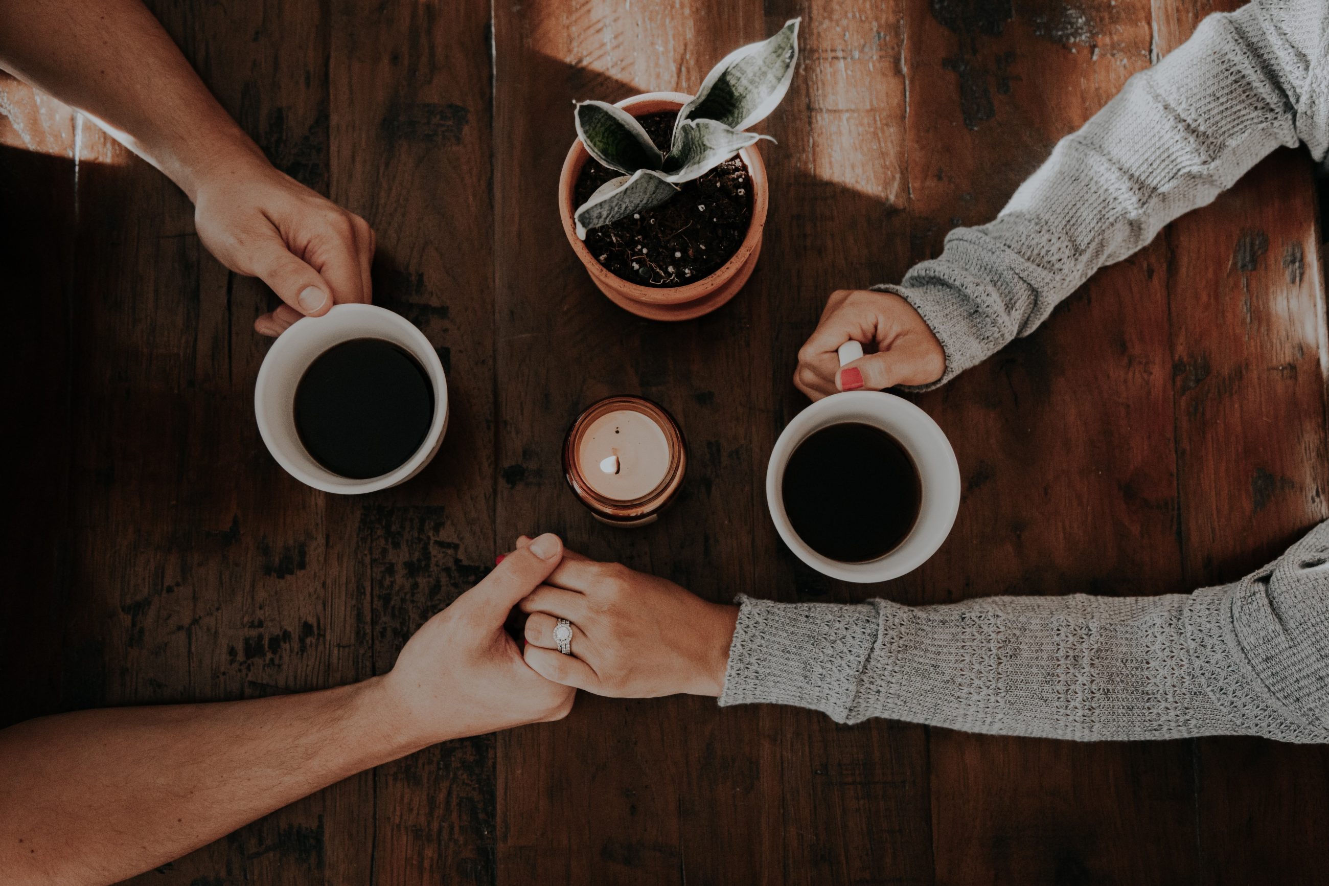 Two people drinking coffee and showing support while holding hands.