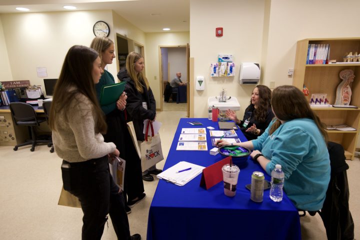 Three students and two nursing representatives going over paperwork at a table.