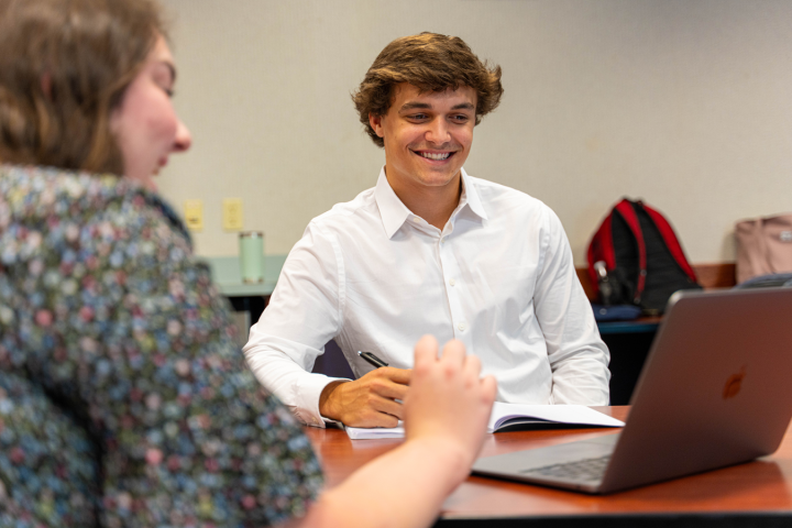 Students smiling around a table observing work on a laptop