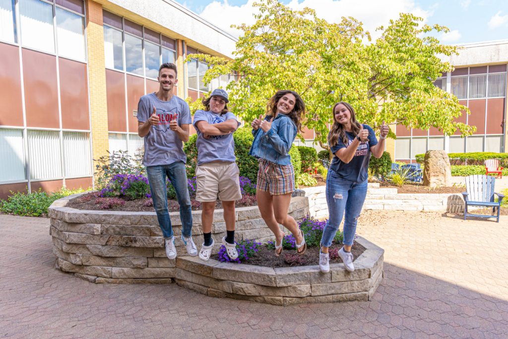 Four students in the Johnson Center courtyard holding a thumbs up mid-air.