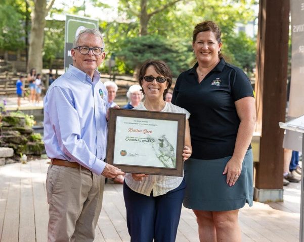 Adjunct professor Kristen Beck holding her Cardinal Award alongside Ohio Governor Mike DeWine and a representative from the Ohio Department of natural Resources.