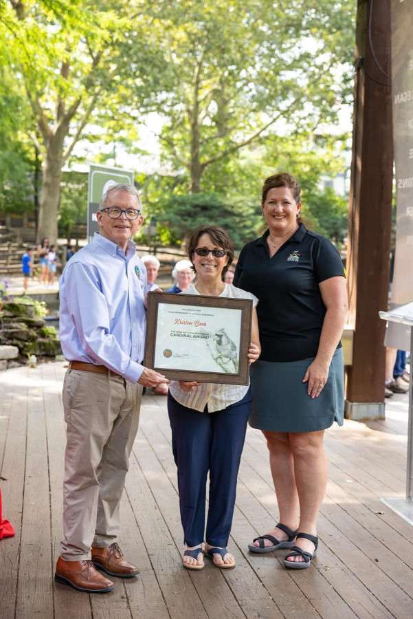 Adjunct professor Kristen Beck holding her Cardinal Award alongside Ohio Governor Mike DeWine and a representative from the Ohio Department of natural Resources.