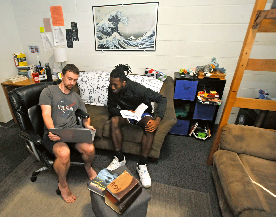 Male student sitting in dorm next to bed with a laptop