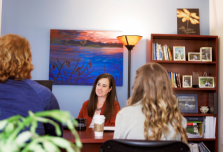 A small group of women sit around a desk in an office