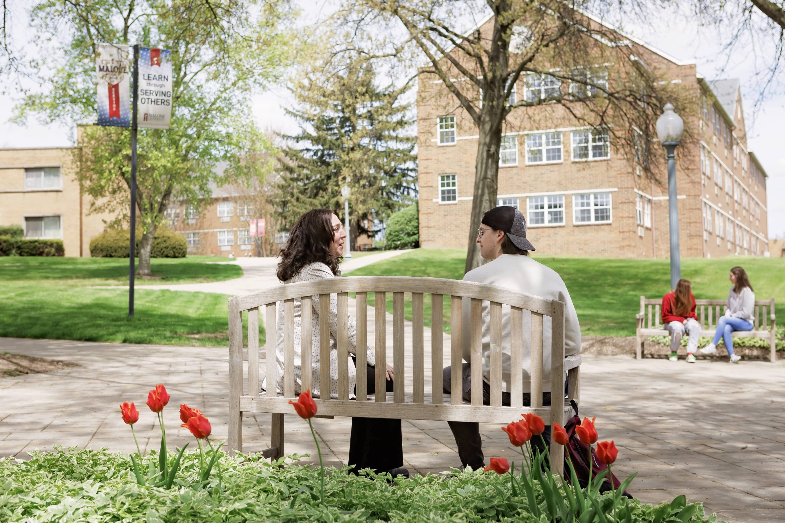 2 people sitting on a bench talking on Malone's campus