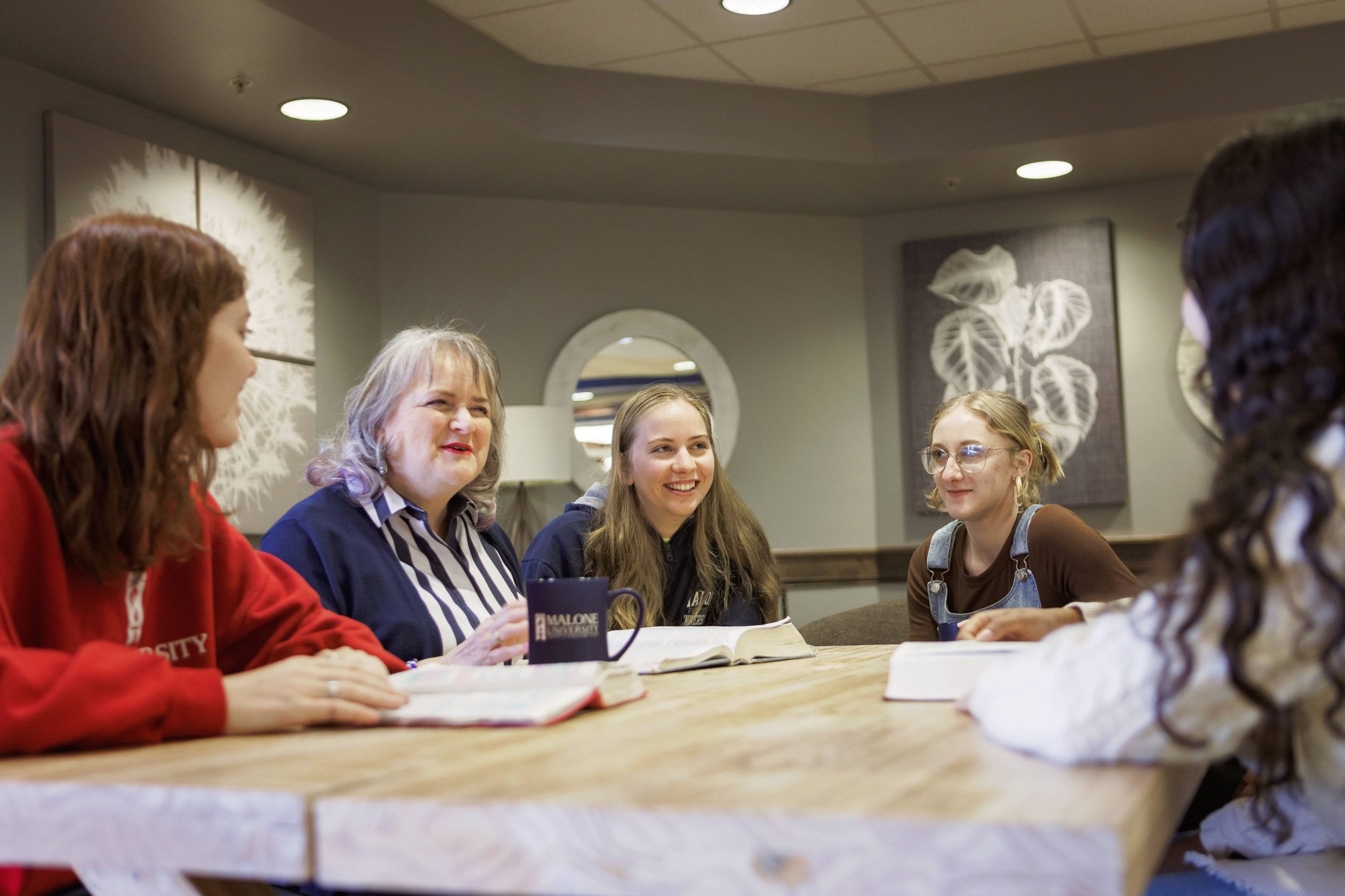 group of 5 women sitting around a table talking