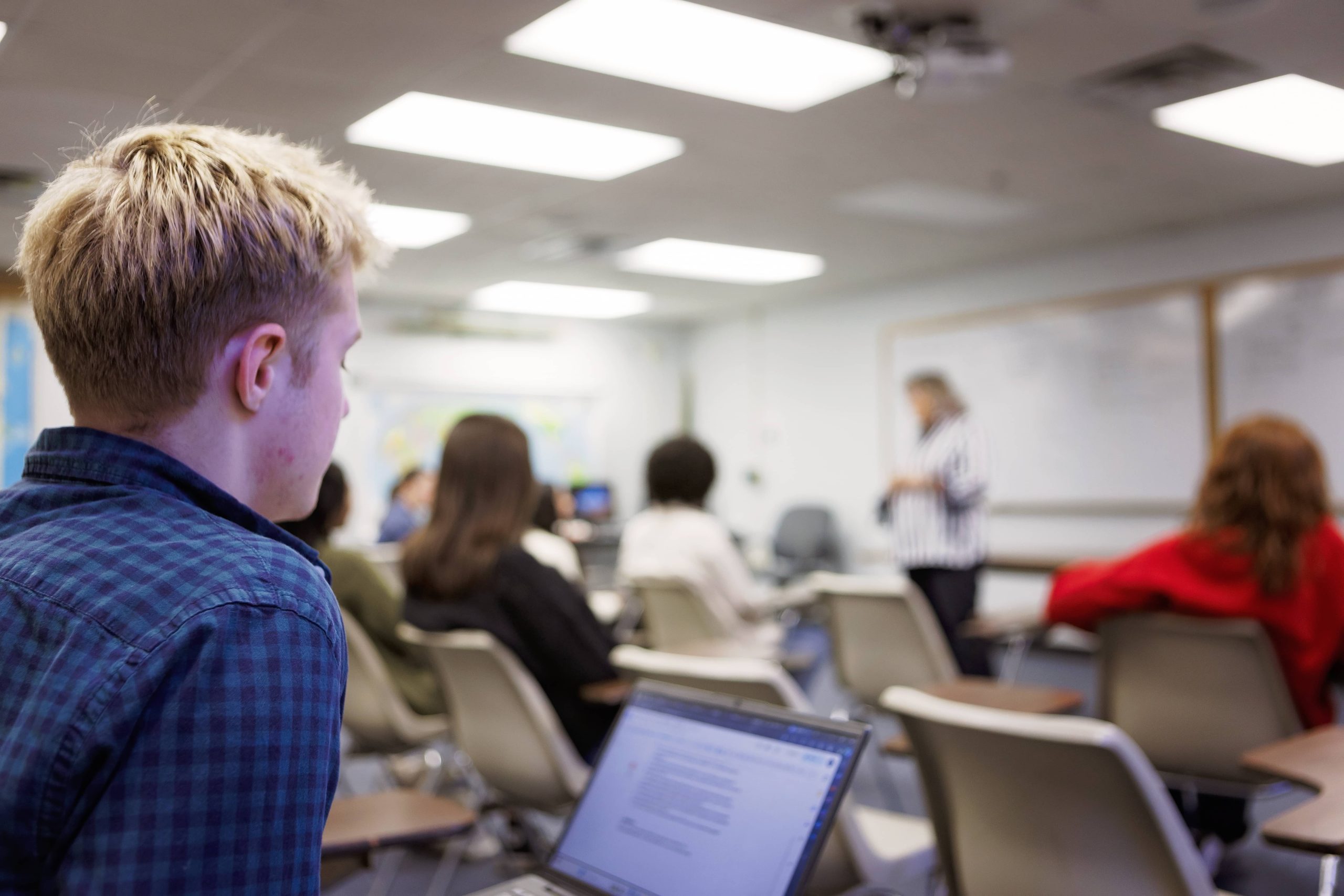student sitting in class listening to instructor with his lap top in front of him