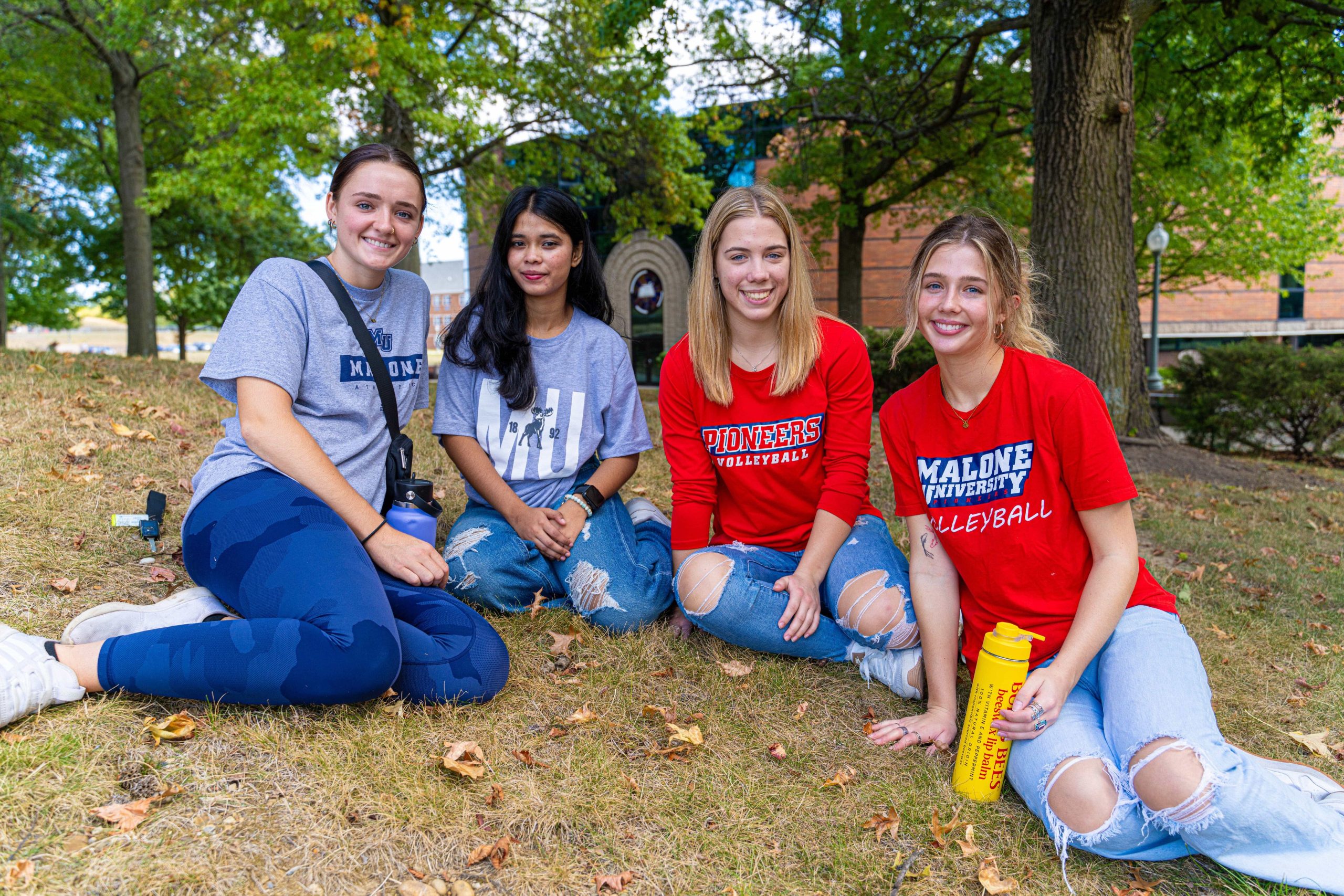 4 female students seated on ground near Cattell Library smiling at camera