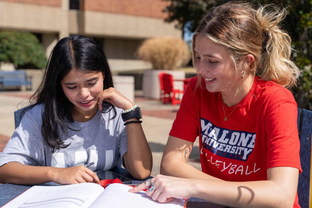 one female student tutoring another at table in front of Cattell Library