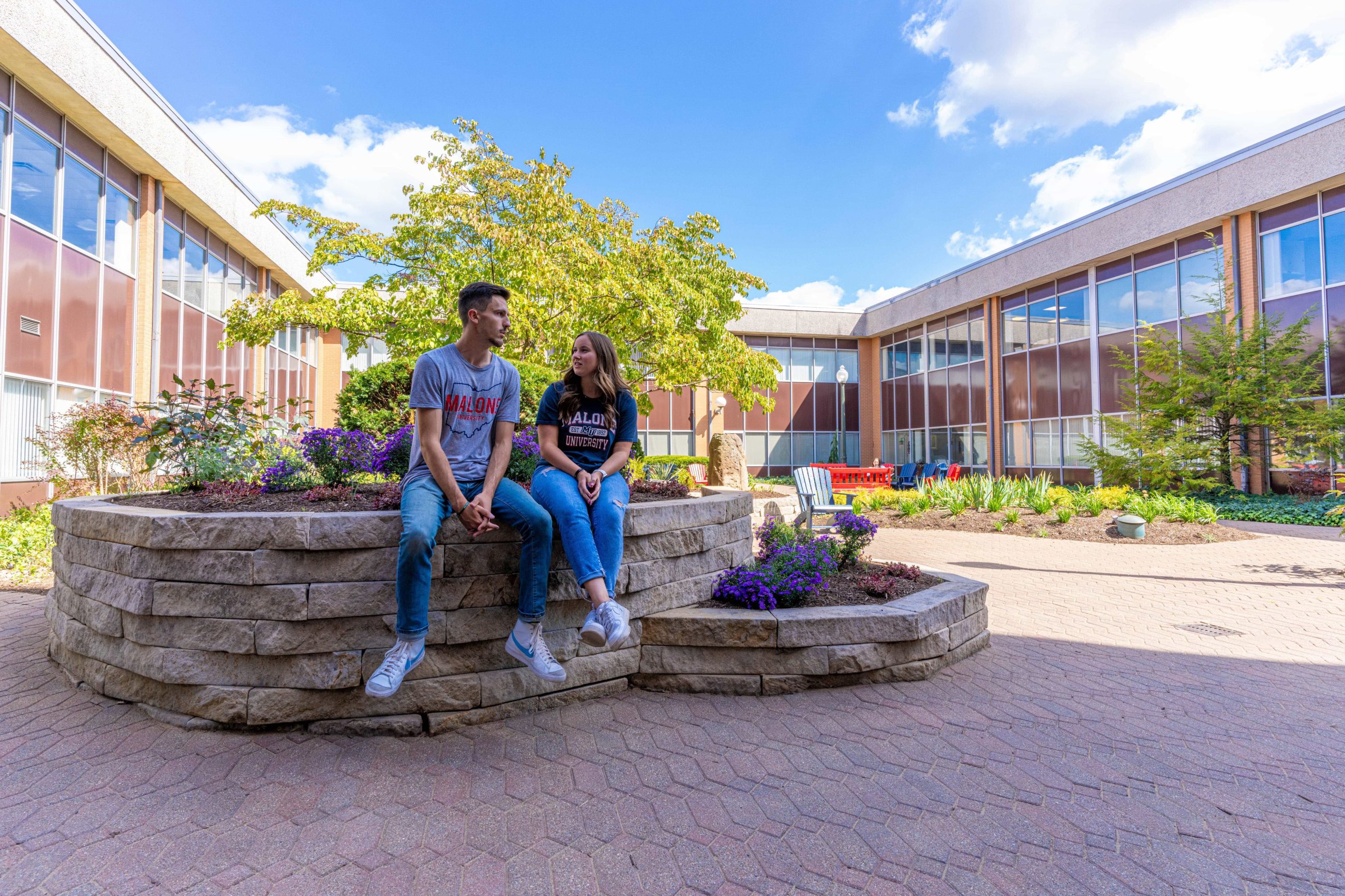 Guy and girl posed on raised wall of flower bed chatting with each other_distance view