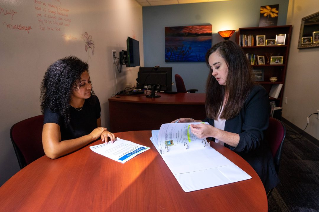 Two women sitting at a table in an office with papers in front of them