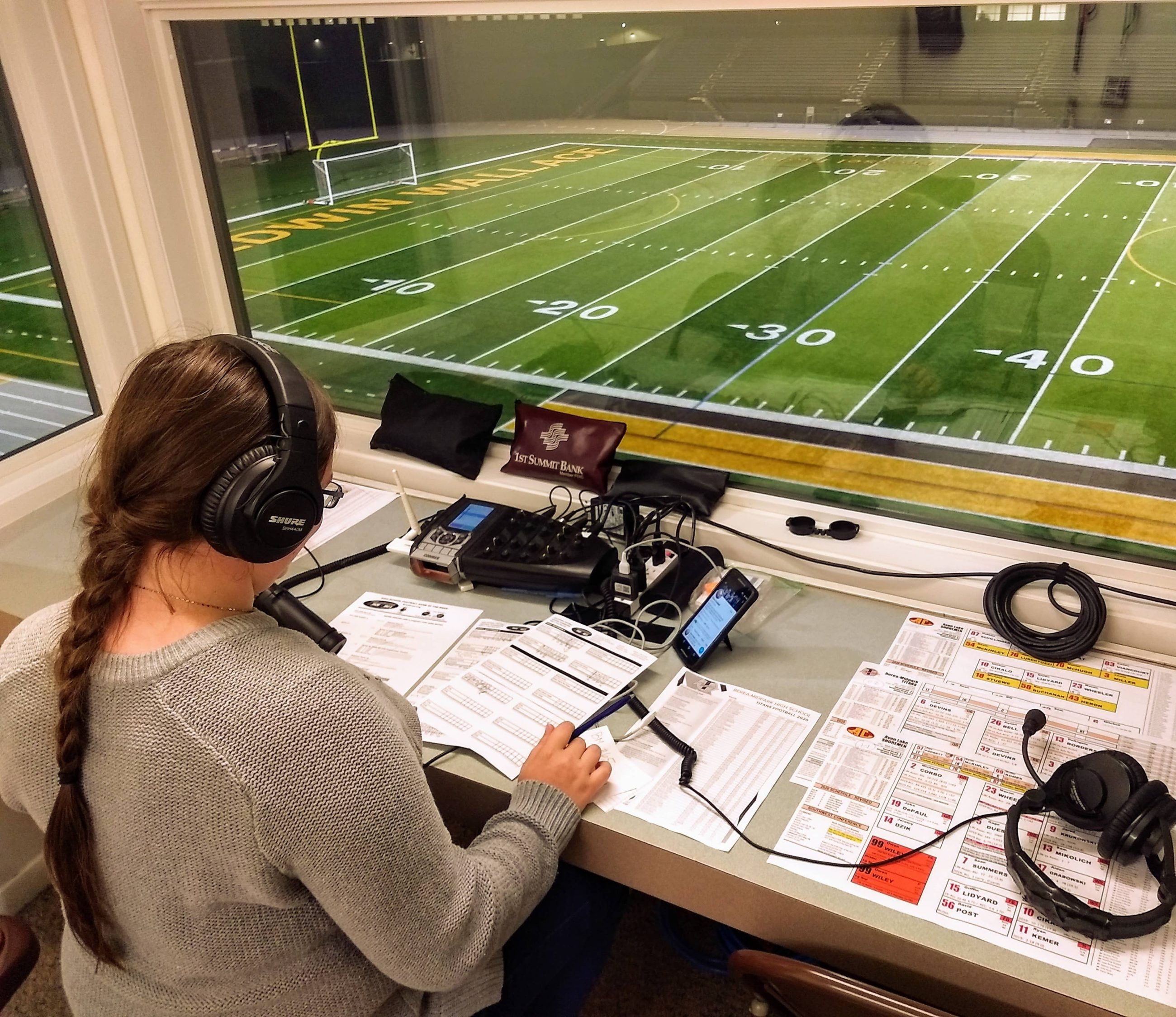 woman with headphones sitting at a desk looking out onto a football field