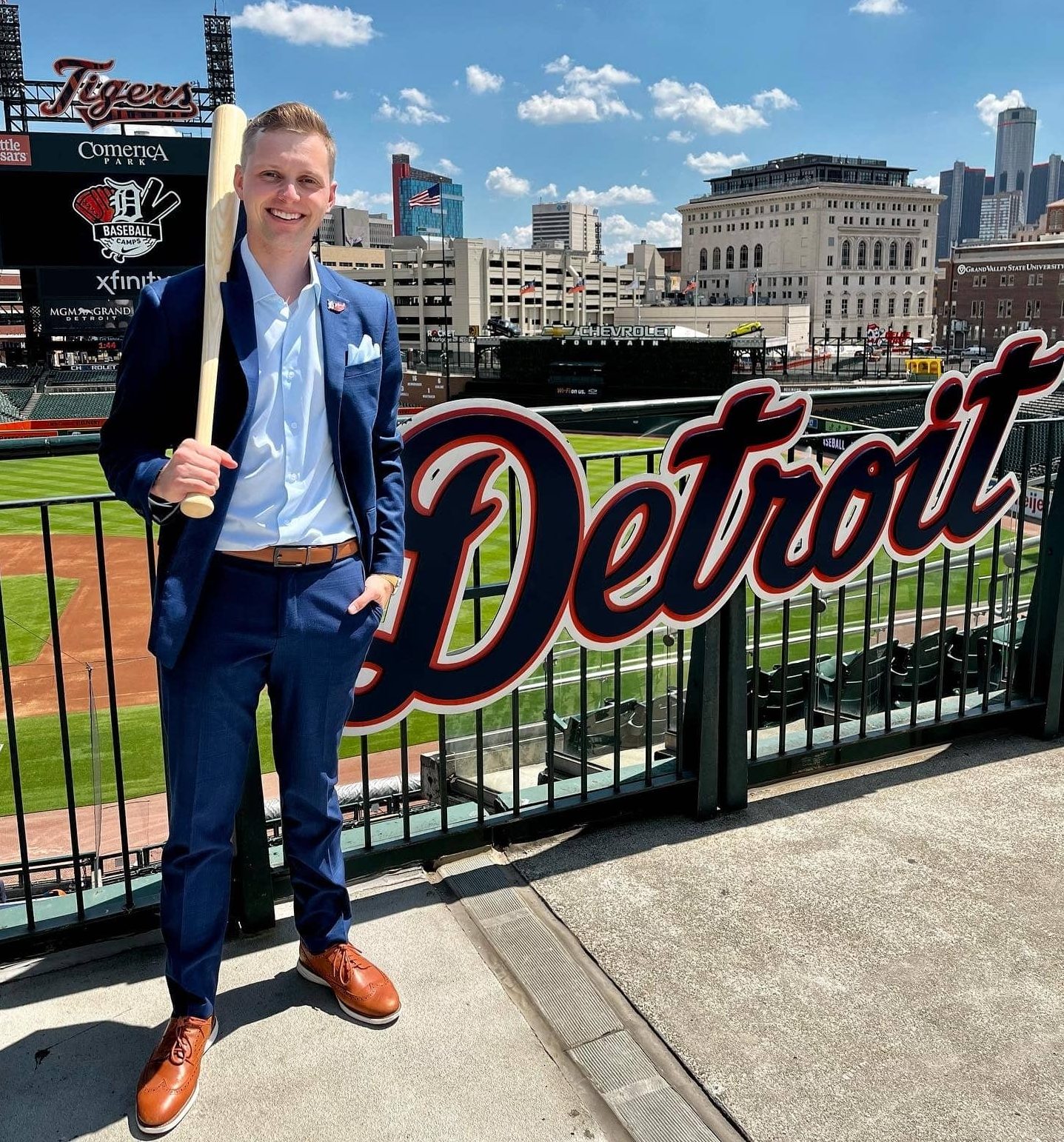 man holding a baseball bat in front of a Detroit sign
