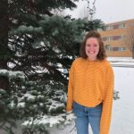 Girl in a yellow striped shirt smiles standing outdoors in snow