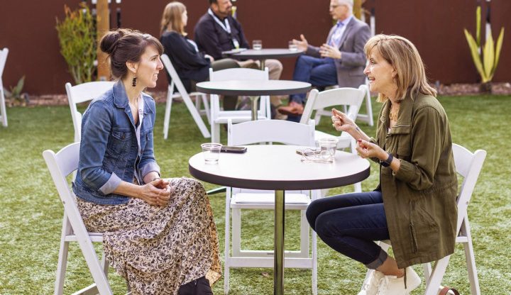 Linda Leon seated at round white table conversing with blond female opposite her
