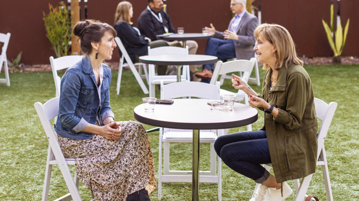 Linda Leon seated at round white table conversing with blond female opposite her