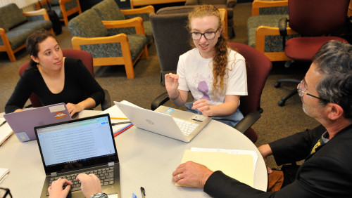 3 people at round table; some laptops in the picture