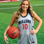 Female student with long hair stands outside in a Malone basketball uniform with basketball