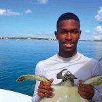 Black male student holds a large turtle while out on the water