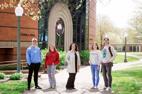 Five Malone students stand outdoors on the sidewalk on a sunny spring day