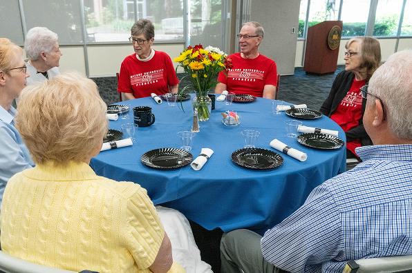 Group of retired Malone supporters sit around a circle table with a blue tablecloth