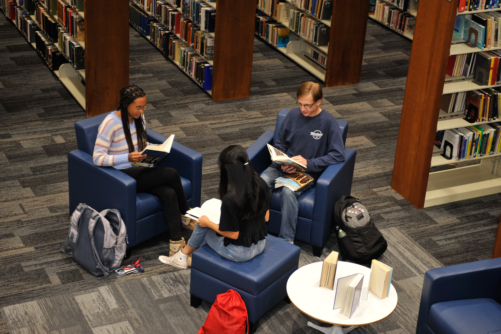 Aerial view of three students sitting in blue chairs in the library