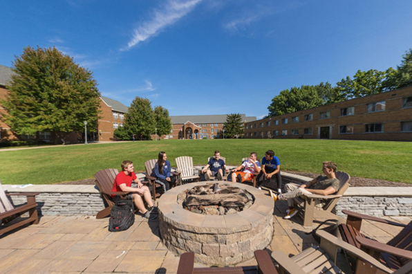 Group of six students sits outside near a fire pit with blue sky above