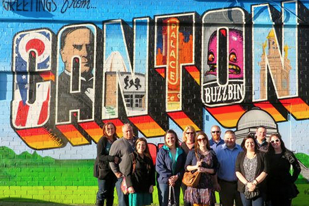 A group of students and parents pose under a mural that reads "Canton" and shows key places around the city