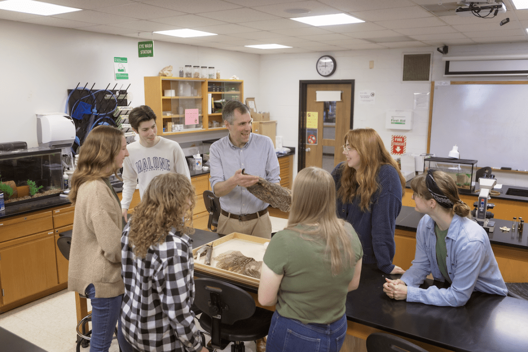 A small group of students gather around a professor inside a class on ornithology wildlife.